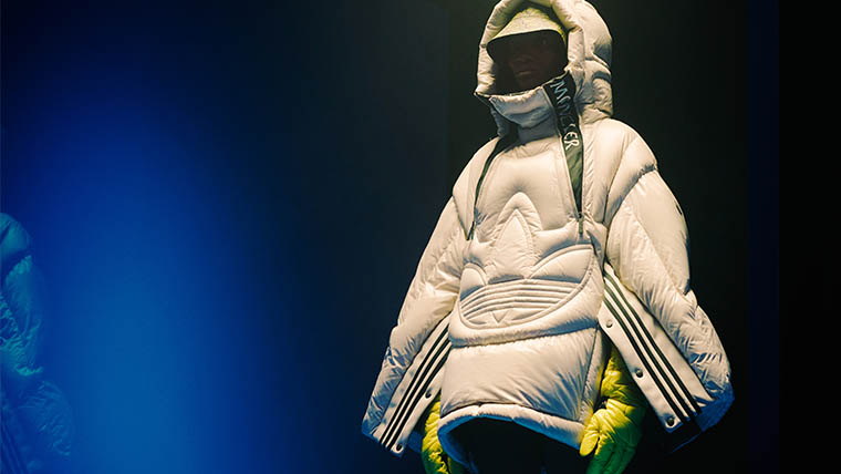 Ein Model trägt eine weiße adidas x Moncler Daunenjacke mit grünen Streifen und gelben Handschuhen (Foto)