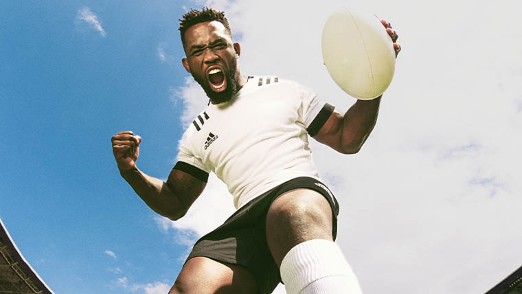 Ein Mann in weißem T-Shirt jubelt mit einem Rugby-Ball in der Hand (Foto)