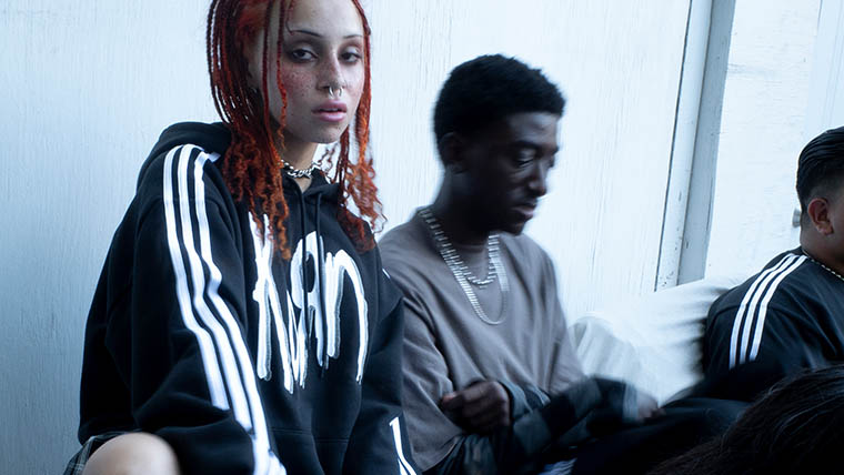 A woman with read hair and a black adidas sweater including the Korn logo sits next to a man wearing a grey t shirt (Photo)