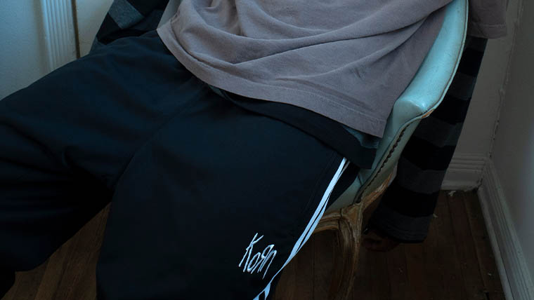 A person is sitting on a chair and wears black adidas x Korn sweat pants (Photo)