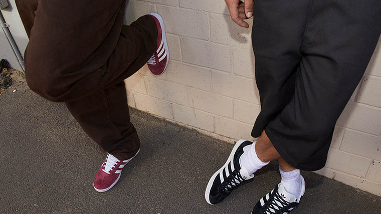 Two people lean against a wall and wear red and black adidas originals shoes (Photo)