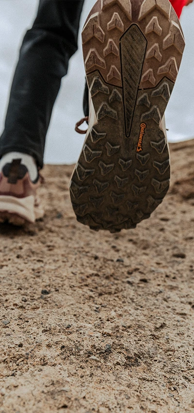 Das Bild zeigt einen Fuß mit einem Wanderschuh, der in einen Erd- oder Kieshaufen getreten ist, was darauf schließen lässt, dass sich die Person im Freien befindet, möglicherweise auf einem Wanderweg oder in bergigem Gelände.