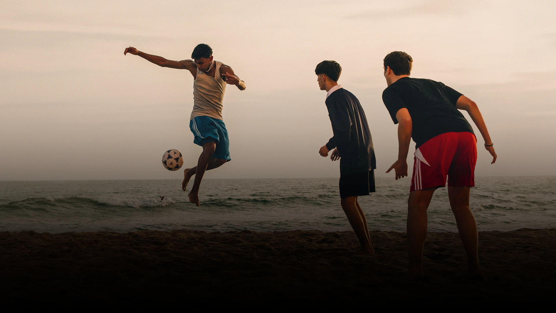 Dieses Foto zeigt Menschen, die bei Sonnenaufgang oder Sonnenuntergang an einem Strand Fußball spielen. Der warme Schein und die Farbsättigung sorgen dafür, dass das Foto einen Moment der Bewegung und Aktivität einfängt, möglicherweise bei einem geselligen Beisammensein oder einer Sportveranstaltung.