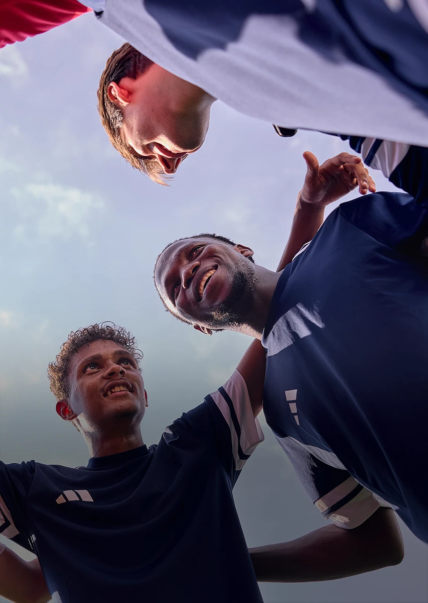 Ein Bild mit einer Gruppe von Menschen, vermutlich Fußballspielern, die Sporttrikots tragen, im Vordergrund stehen und mit gefalteten oder über den Schultern verschränkten Armen posieren.