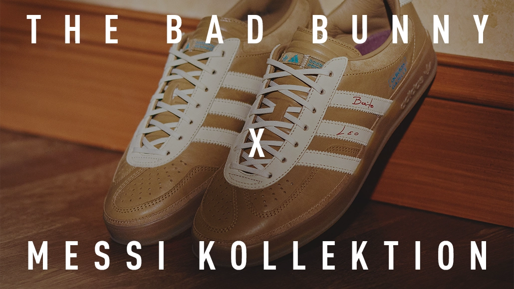 Das Bild zeigt ein Paar goldene Adidas-Sneaker, die vor einer Wand stehen. Der Hintergrund ist verschwommen, aber es scheint sich um eine Innenkulisse zu handeln. Unter den Schuhen steht der Schriftzug „THE BAD BUNNY X MESSI COLLECTION“, was darauf schließen lässt, dass diese Schuhe mit der Bad Bunny-Kollektion in Verbindung stehen, möglicherweise mit Merchandise oder Accessoires, die mit dem Künstler in Verbindung stehen.