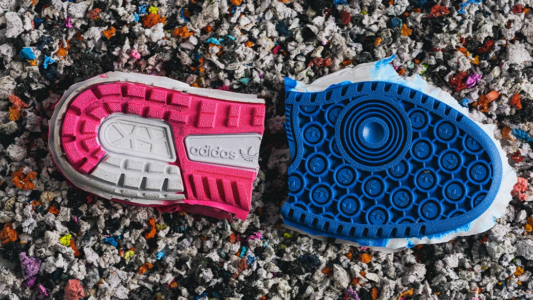 A collage image showing two different sneaker soles placed on multicolored shredded paper. The left sole is pink-colored and the right is blue. 