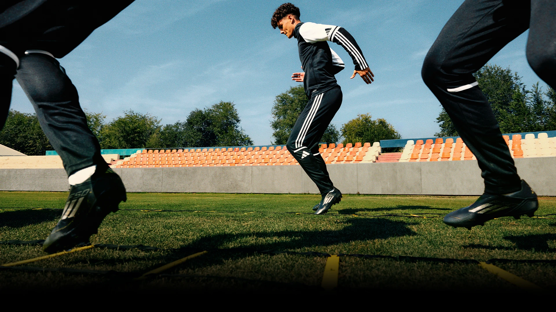 This is an image featuring three soccer players training on a track. They are wearing athletic attire, suggesting they are athletes participating in a training session.