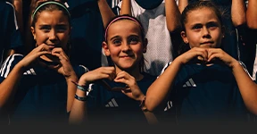 The image shows a group of people posing together. They appear to be young athletes - children, possibly part of a soccer or volleyball team, given the sportswear and equipment visible in the background.