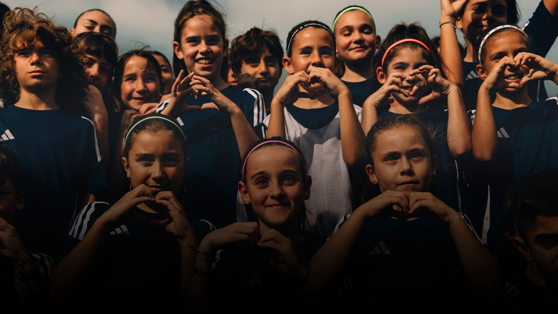 The image shows a group of people posing together. They appear to be young athletes - children, possibly part of a soccer or volleyball team, given the sportswear and equipment visible in the background.