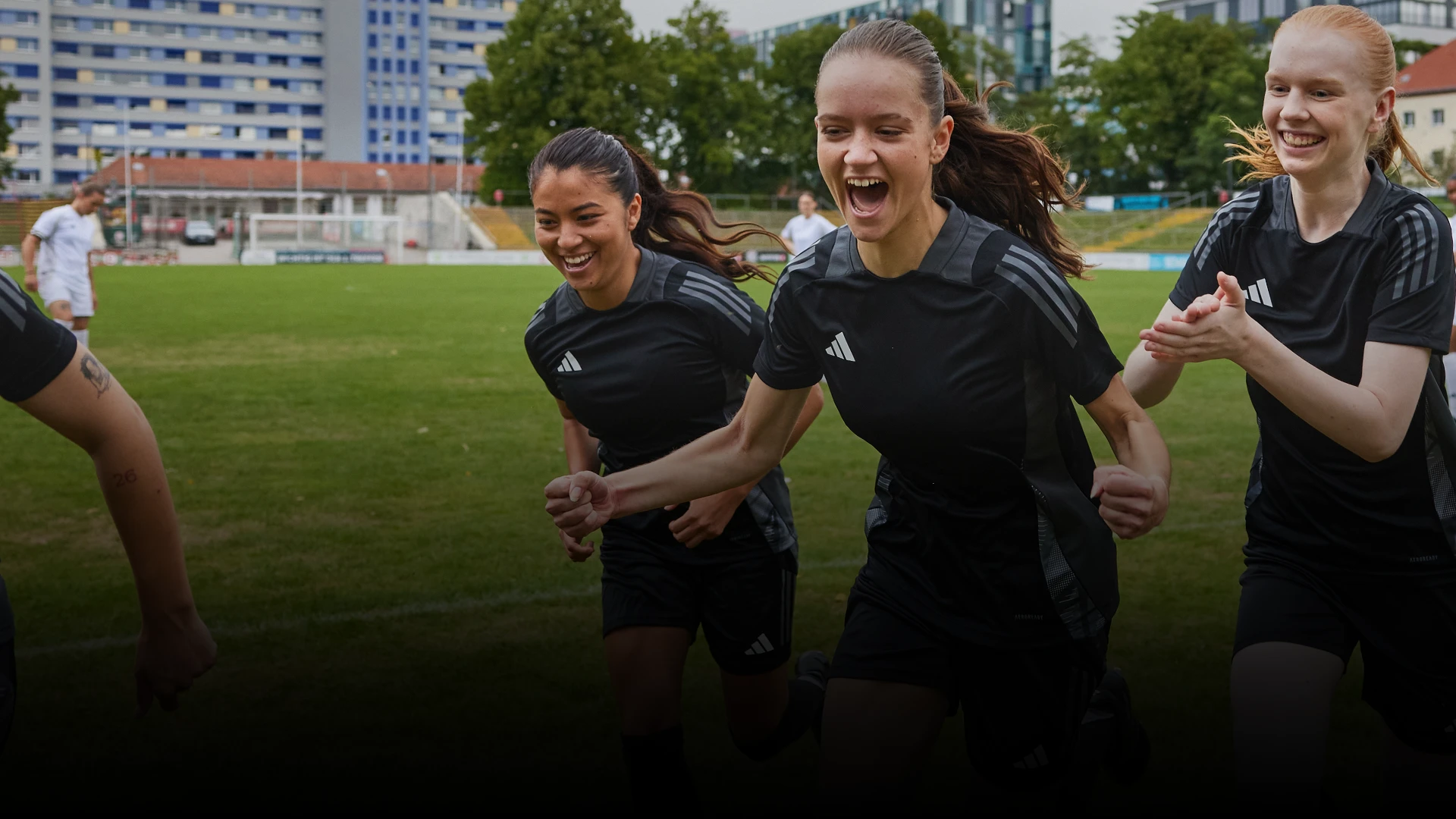 The image shows a group of female athletes. They are running on a soccer field, looking joyfully. There's a sense of camaraderie and celebration, as they all appear to be smiling and enjoying a moment together.