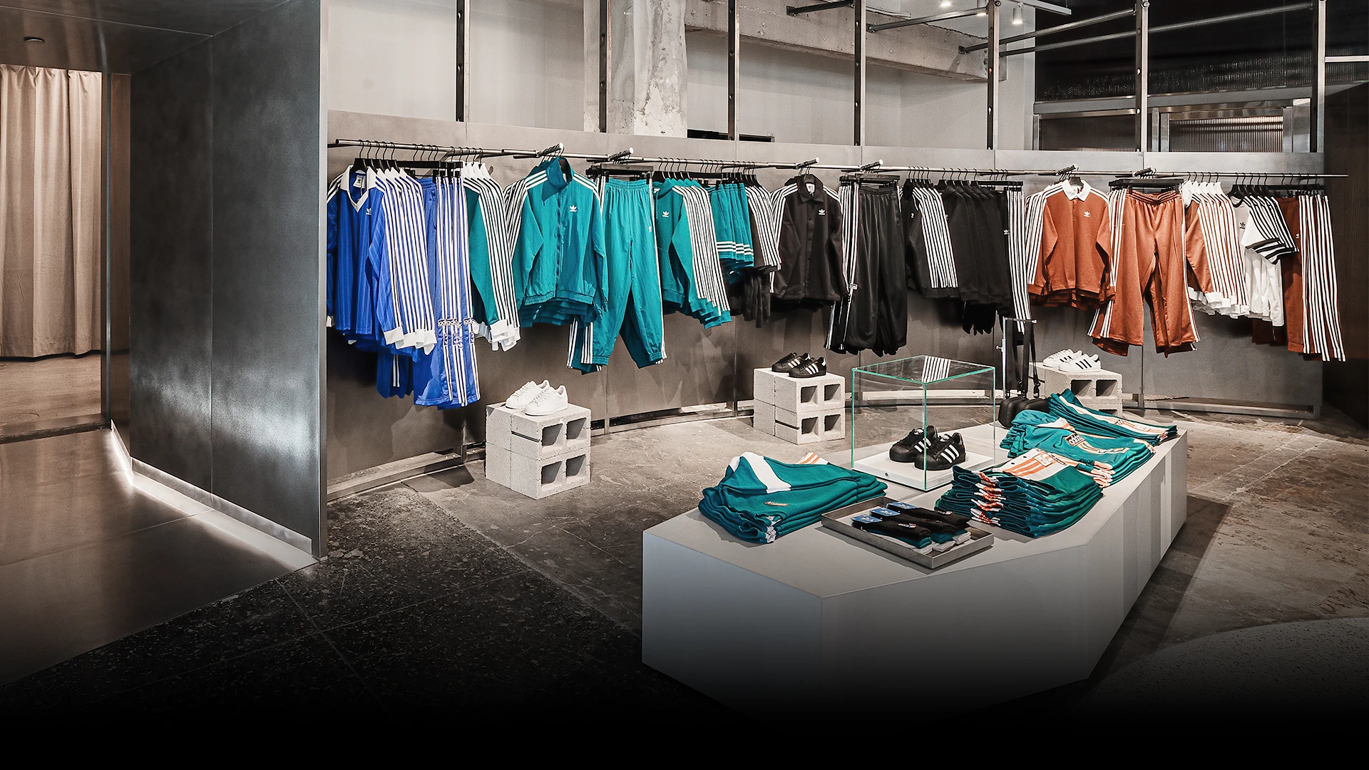 The image shows an interior view of an adidas store. There is a variety of jackets and other sportswear displayed on the walls The color scheme of the items primarily consists of dark and light colors with striped patterns.