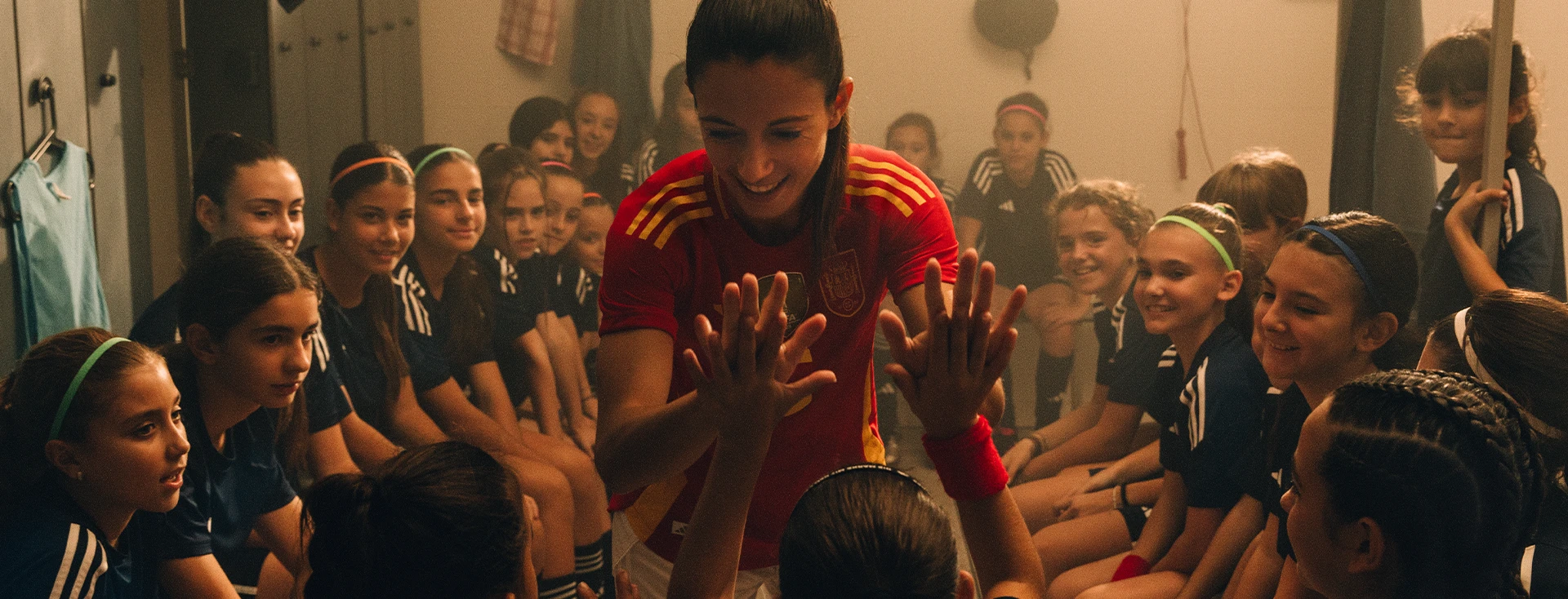 The image shows a group of people, mostly children, appearing to be either participating in or observing some form of activity. In the center, there's an adult female figure - possibly their coach - who seems to be giving instructions or motivating the group, as indicated by his gesture and raised hands.