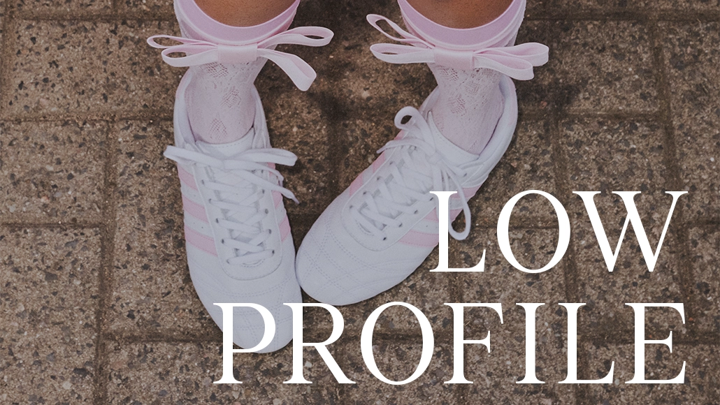 This is an image with a person's legs, wearing sneakers and pink socks. The background shows a tiled floor. There is text on the image that reads "LOW PROFILE".