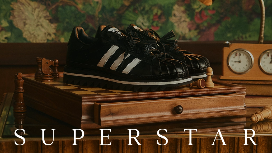 The image shows a pair of Adidas sneakers resting on a wooden surface with the word "SUPERSTAR" below it.