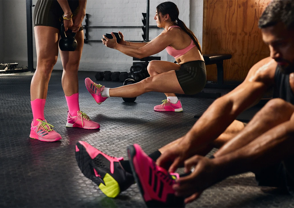 The image shows a gym setting where three individuals are exercising.