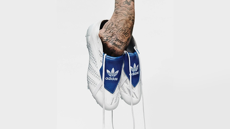 The image shows a pair of adidas shoes with one the adidas logo facing outward. In the center, there is an object that appears to be hands reaching out towards the shoes.