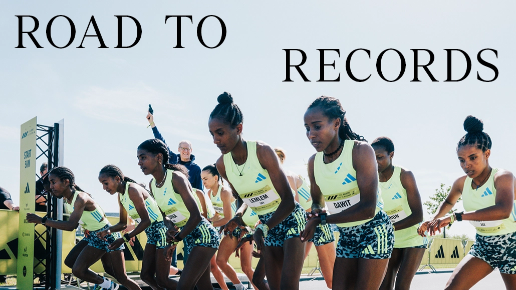 A photo is a group of athletes posing together at what seems to be a race finish or a starting point, all wearing racing bibs with numbers on them. 