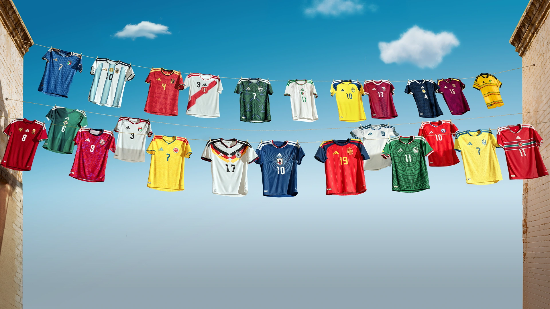 Mehrere internationale adidas Fußballtrikots hängen an Wäscheleinen zwischen zwei Gebäuden vor blauem Himmel. (Foto)