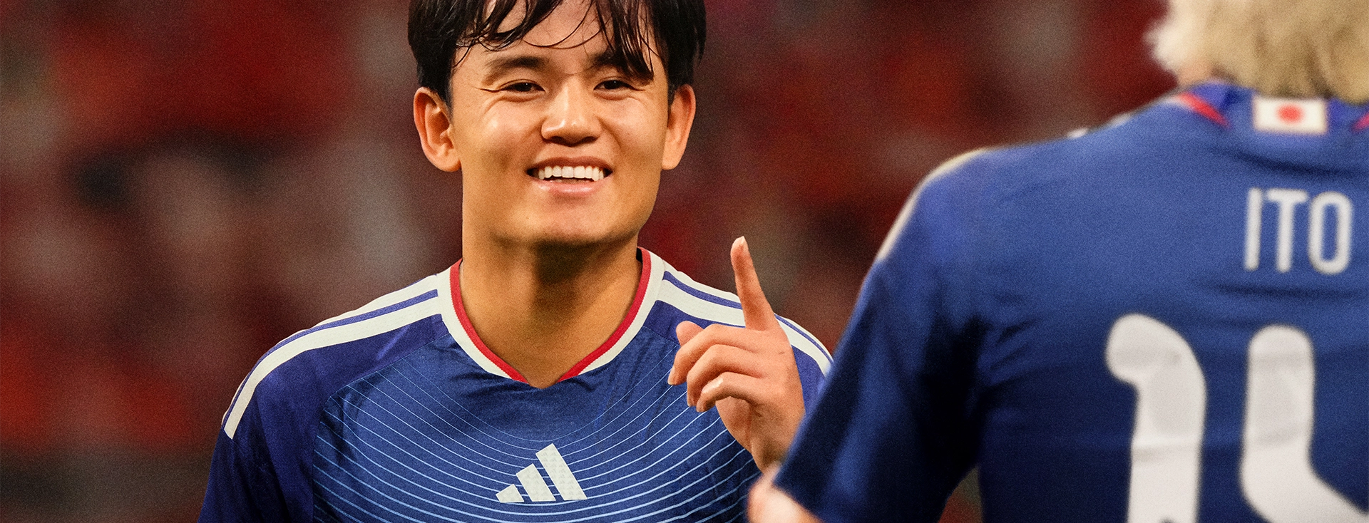 Fußballspieler im blauen Japan-Trikot von adidas lächelt im Stadion. (Foto)