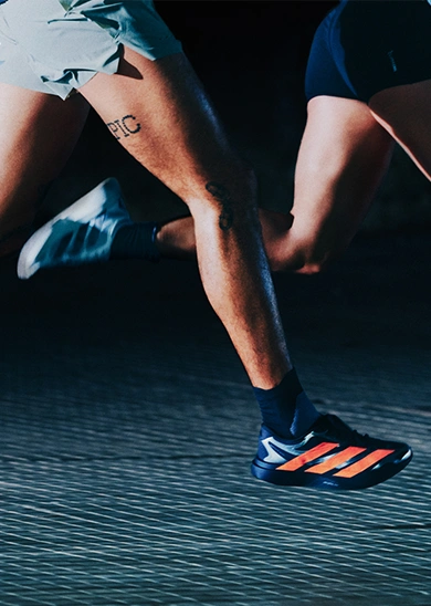 Two runners wearing adidas shoes in motion on a dark surface. (Photo)