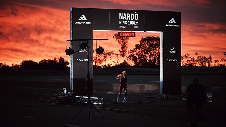 Male runner under a “Nardò Ring 100km” finish arch at sunset, with a digital time display visible. (Photo)