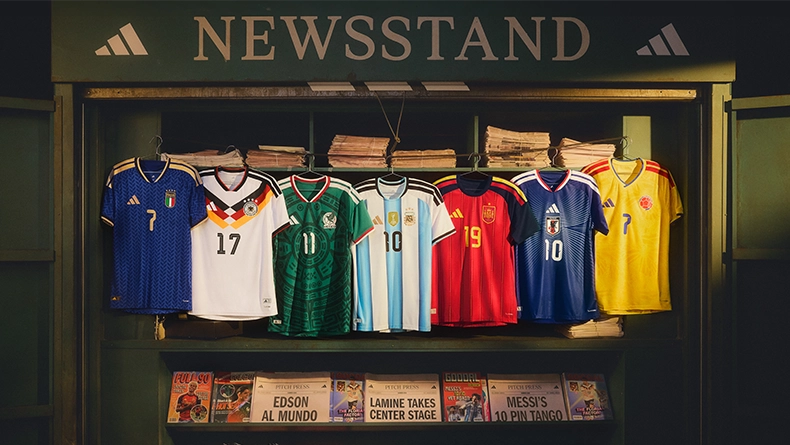 National team football jerseys displayed in a lit kiosk labeled “Newsstand,” with newspapers and magazines placed below. (Photo)